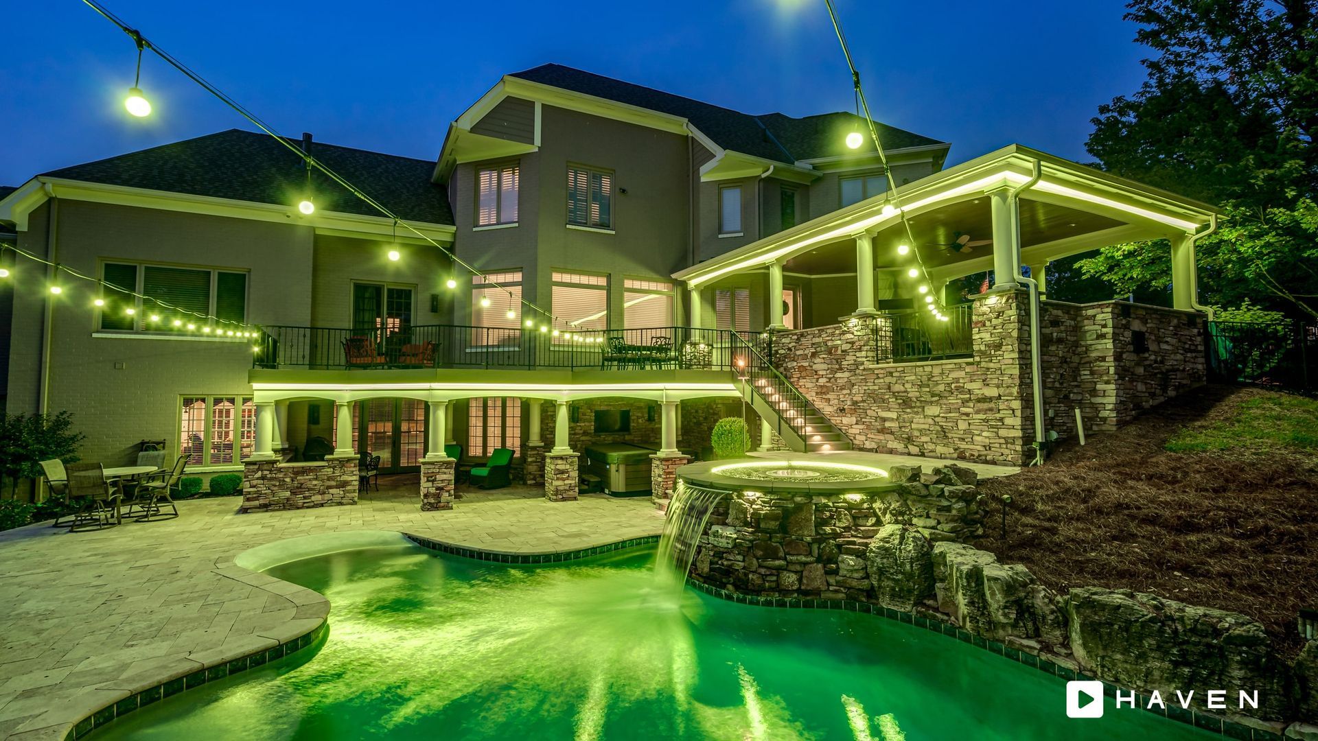 A large house with a swimming pool in front of it at night.