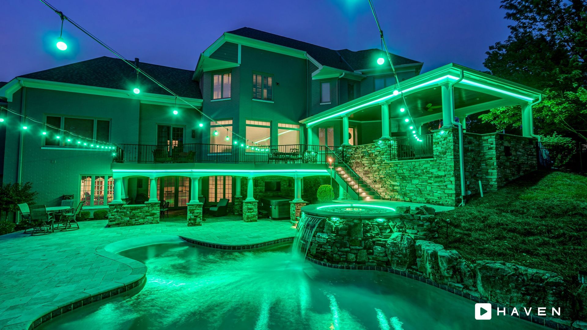A large house with a swimming pool is lit up with green lights at night.