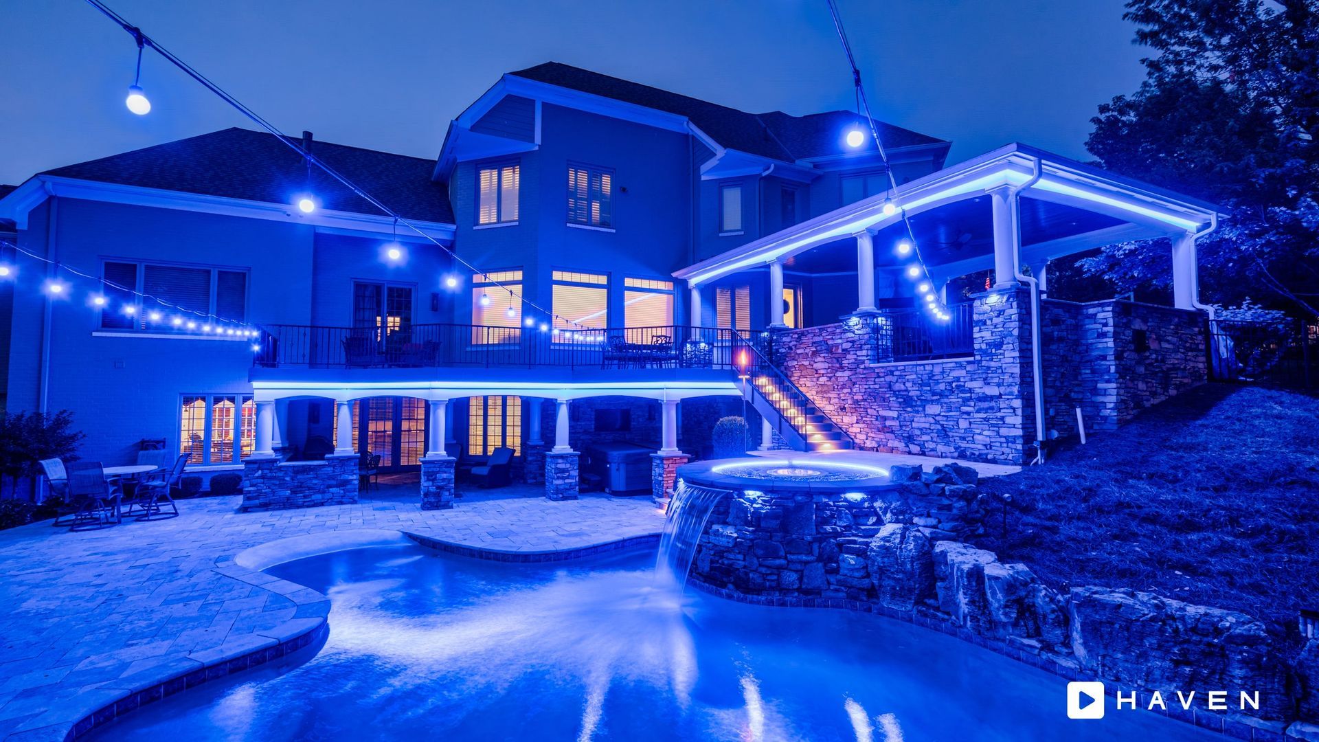 A large house with a pool in front of it is lit up with blue lights.