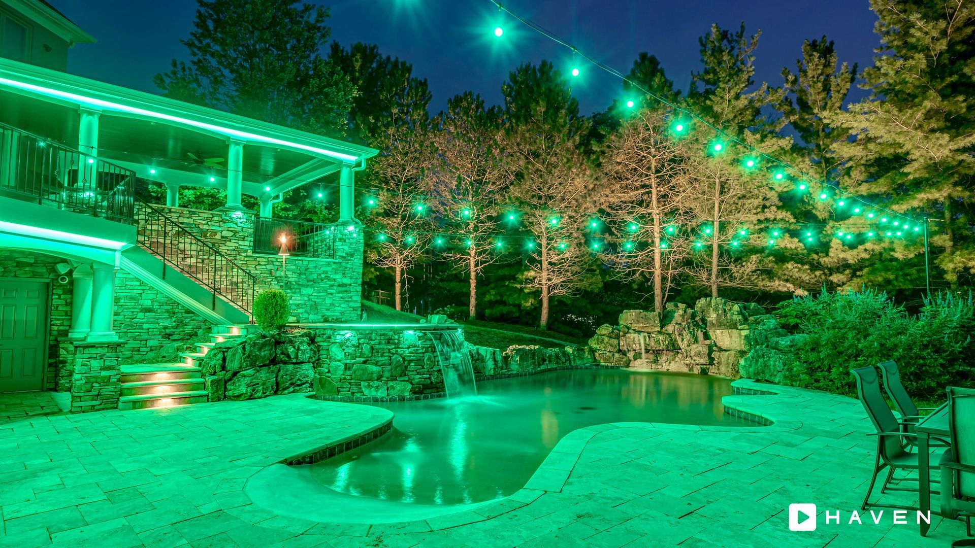 A swimming pool is lit up with green lights in a backyard.