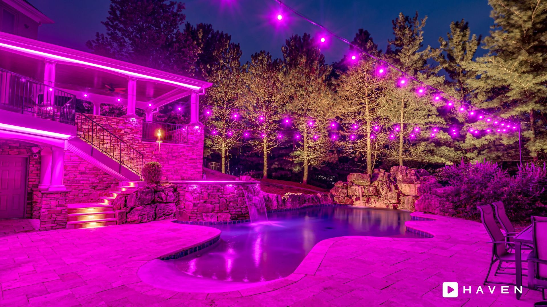 A swimming pool is lit up with purple lights in front of a house.