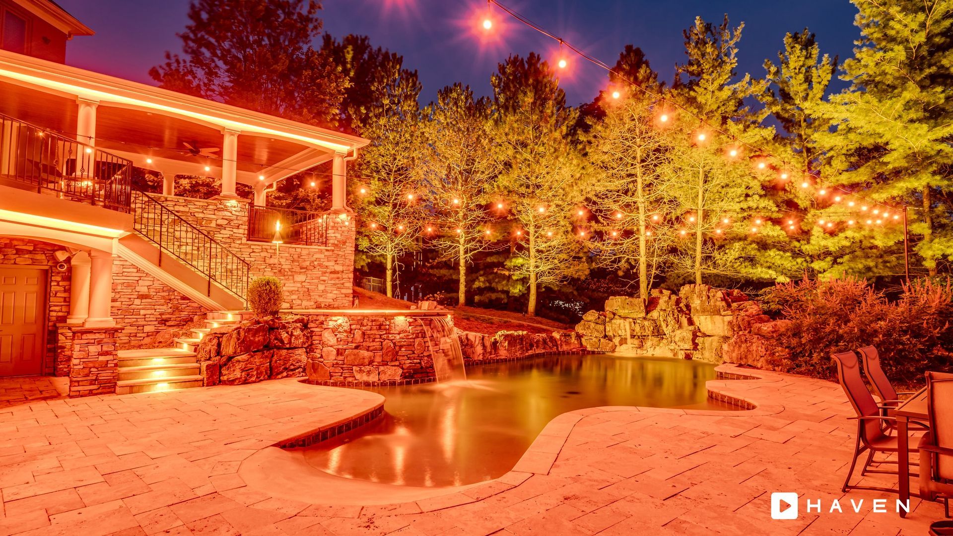A large house with a swimming pool in front of it is lit up at night.