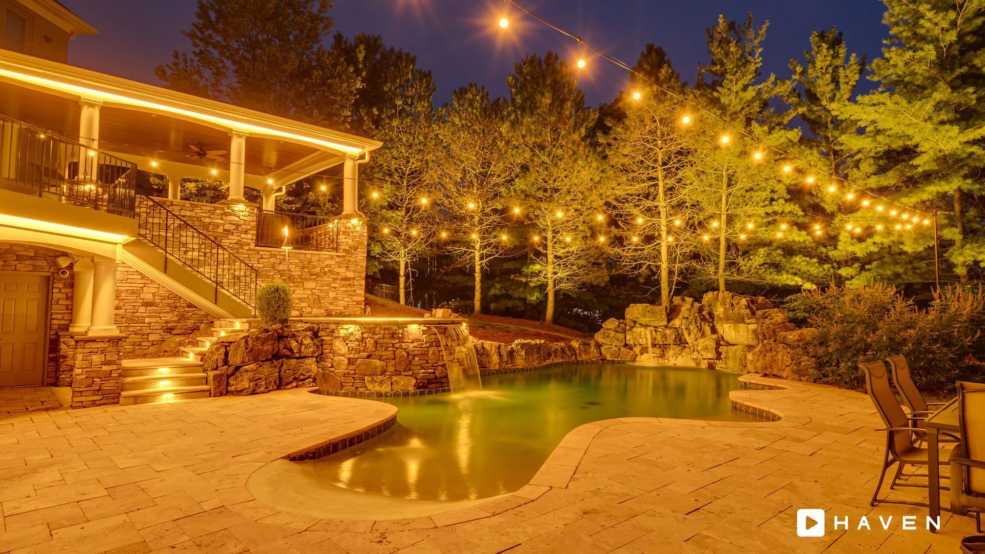 A swimming pool is lit up at night in front of a house.