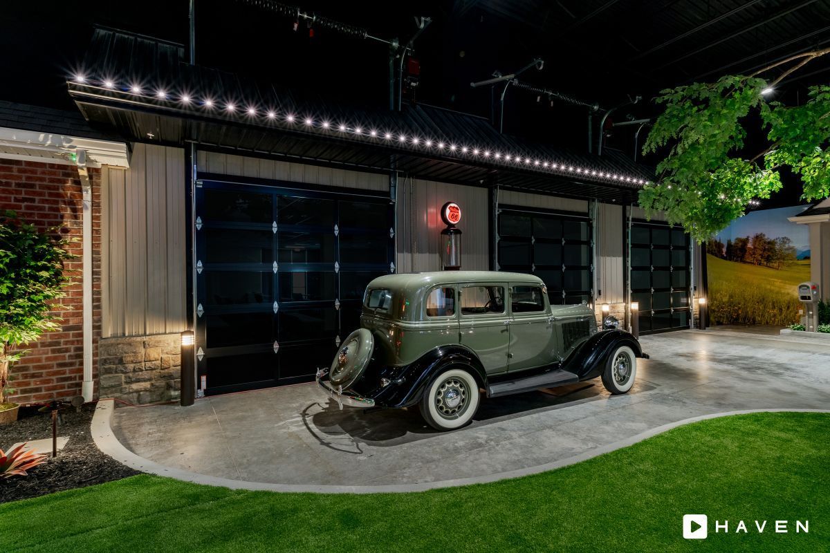 An old car is parked in front of a garage at night.