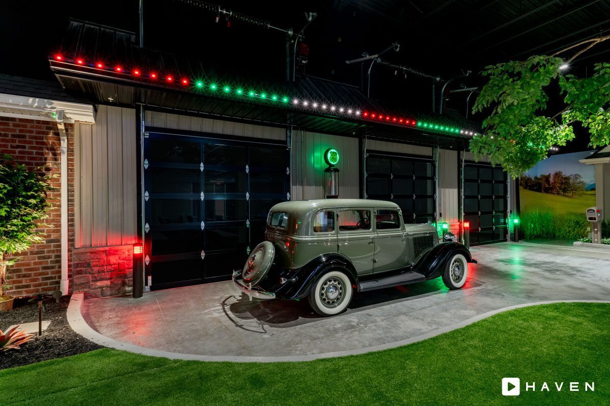 An old car is parked in front of a garage with christmas lights.