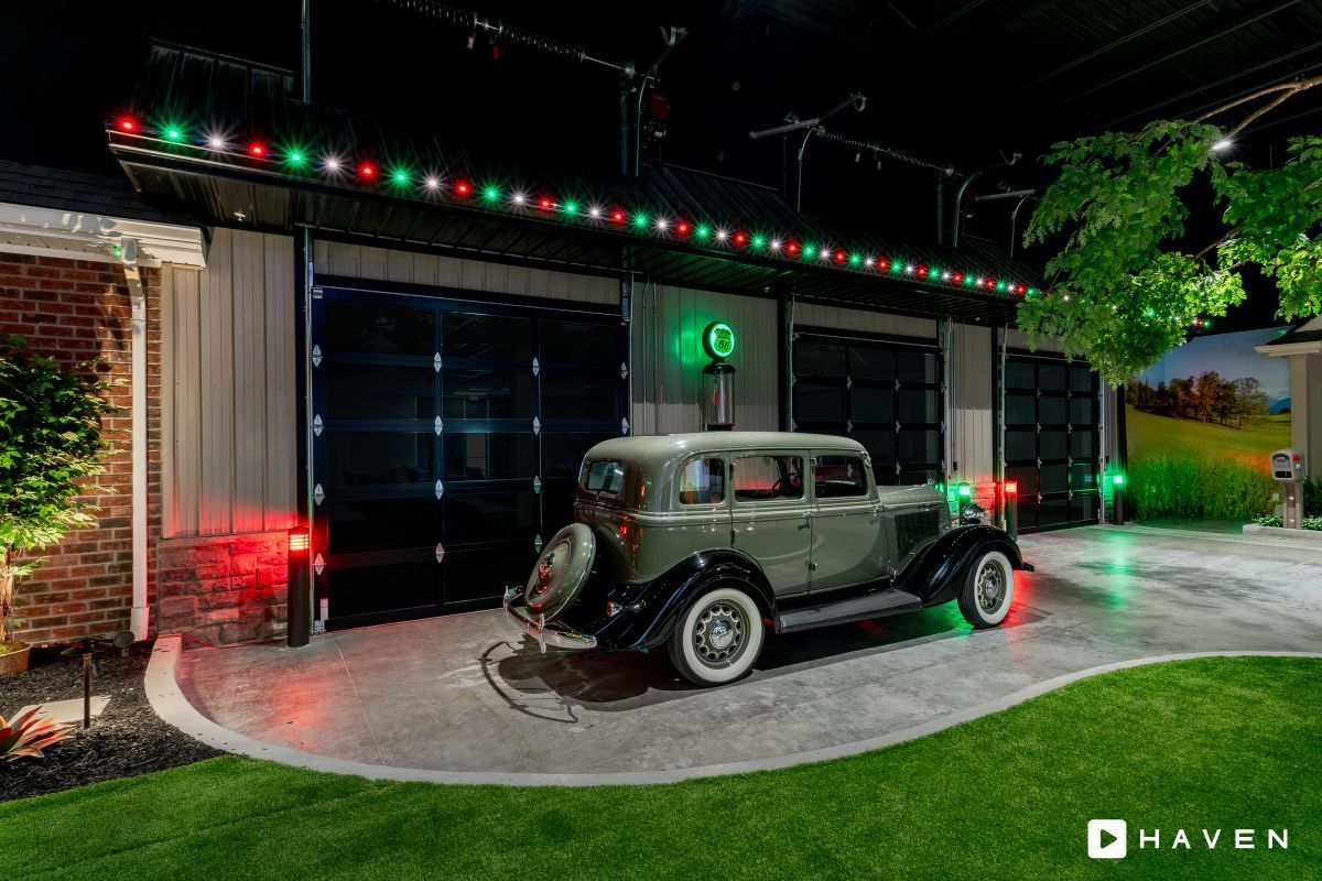 An old car is parked in front of a garage with christmas lights.