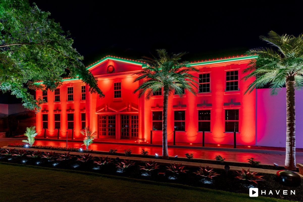 A large, illuminated red building at night, flanked by palm trees and green landscaping.