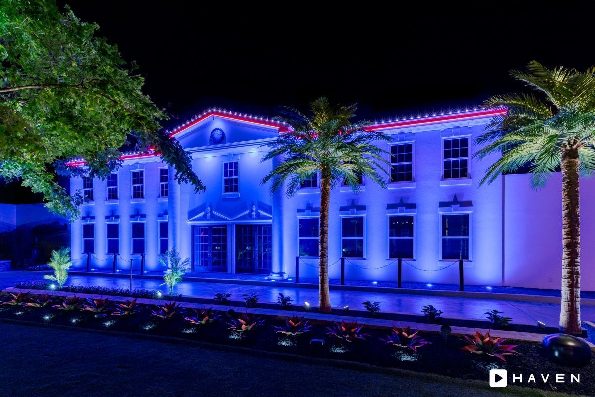 A large white building is lit up with blue lights at night.