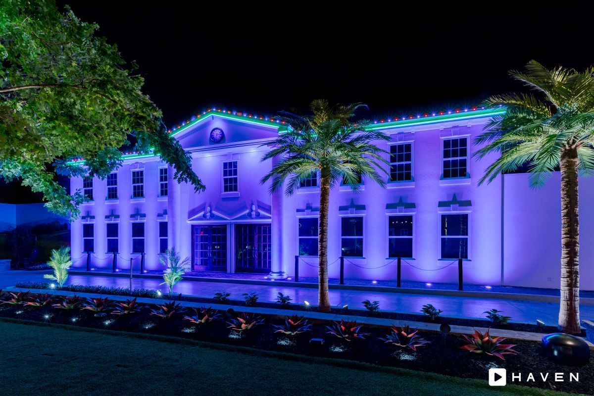A large white building is lit up with purple lights at night.