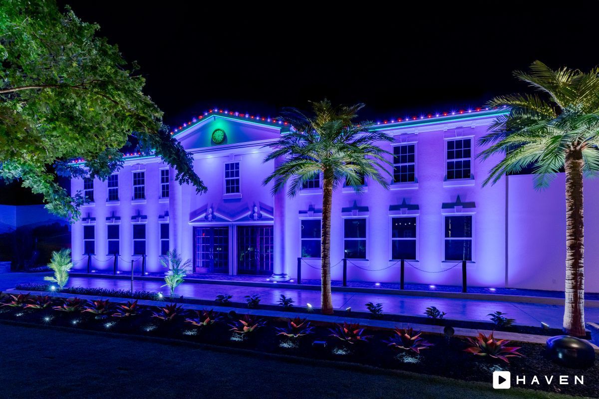 A large white building is lit up with purple lights at night.