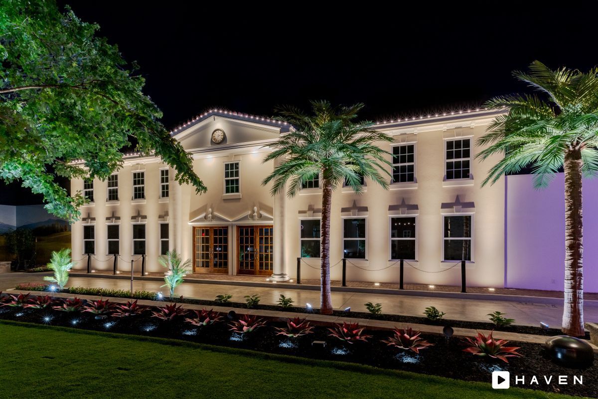 A large white building is lit up at night with palm trees in front of it