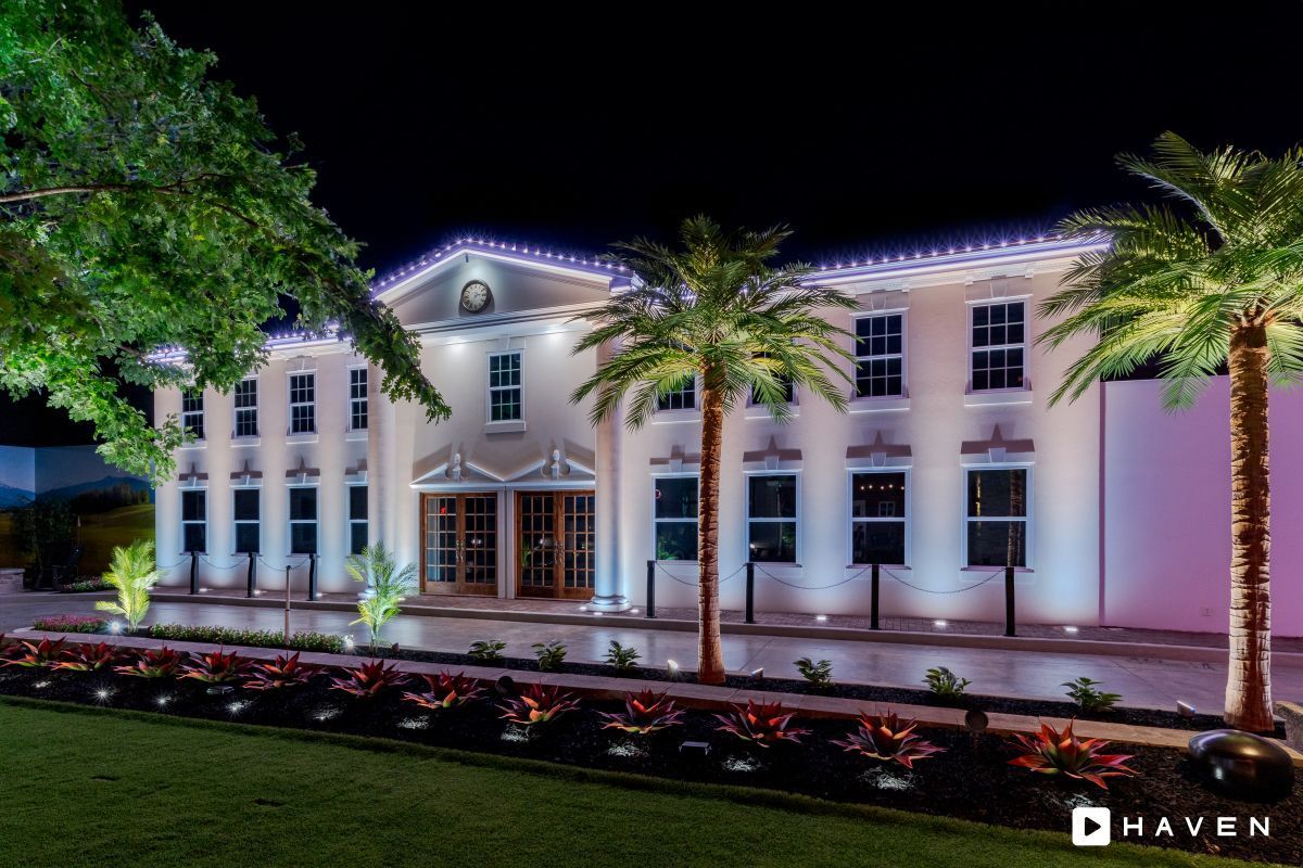 A large white building is lit up at night with palm trees in front of it