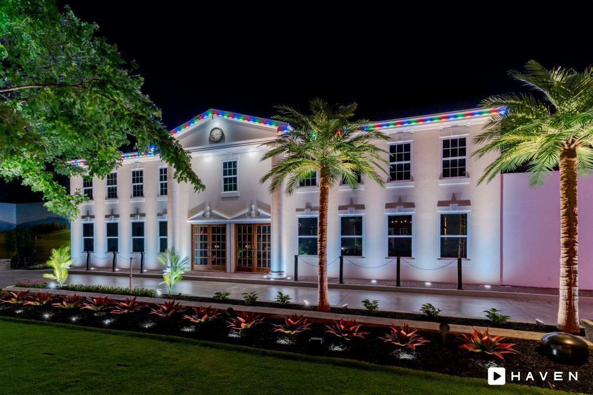 A large white building is lit up at night with palm trees in front of it.