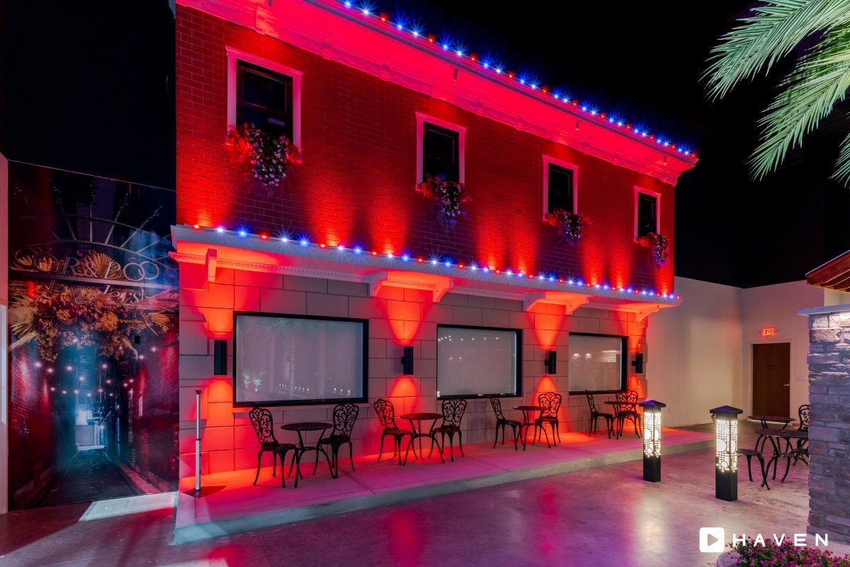 Exterior of a red-lit building with outdoor seating at night, illuminated with red and blue lights.