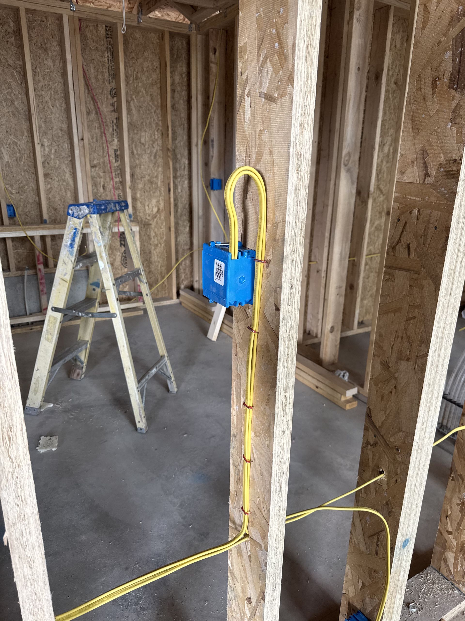 Electrical wiring in blue box on wooden framing of a building under construction. Yellow wires are visible.