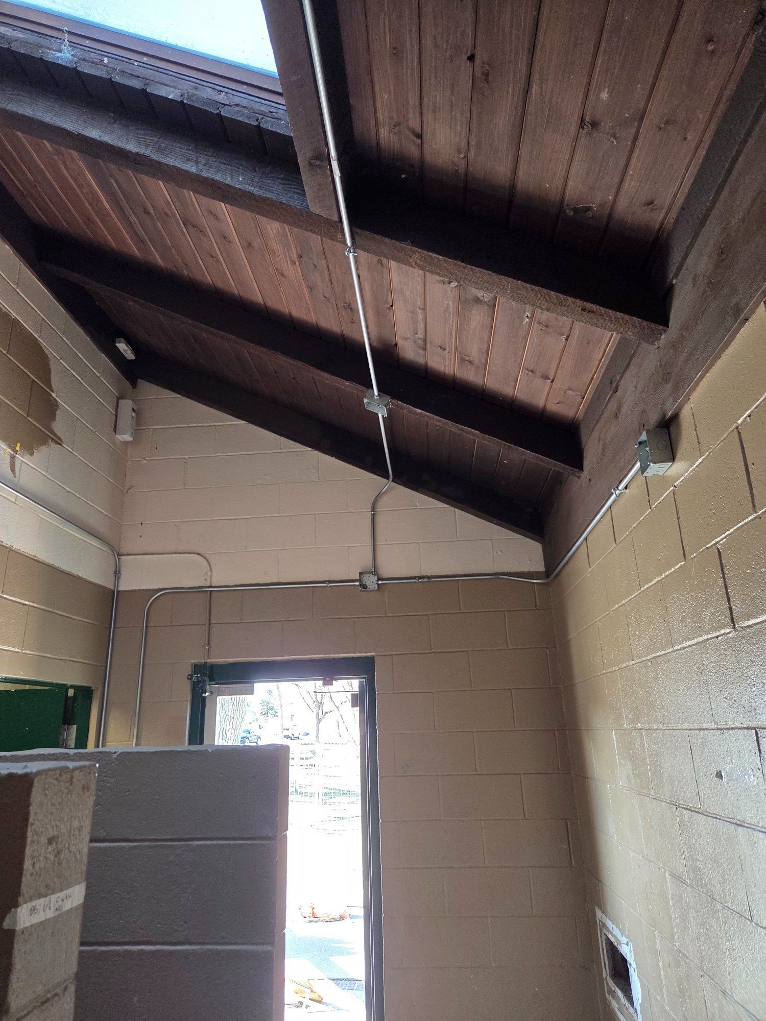 Interior of a building with a wooden sloped ceiling and exposed beams, a doorway, and concrete block walls.
