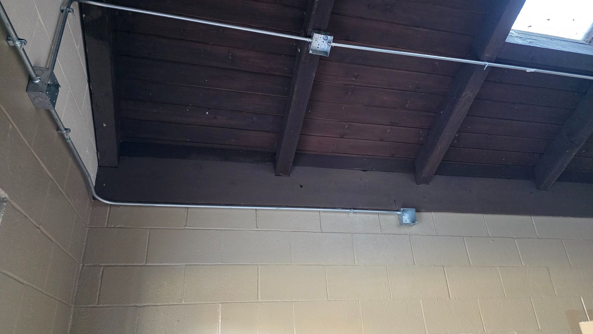 Electrical conduit runs along a brown wooden ceiling and tan brick wall.