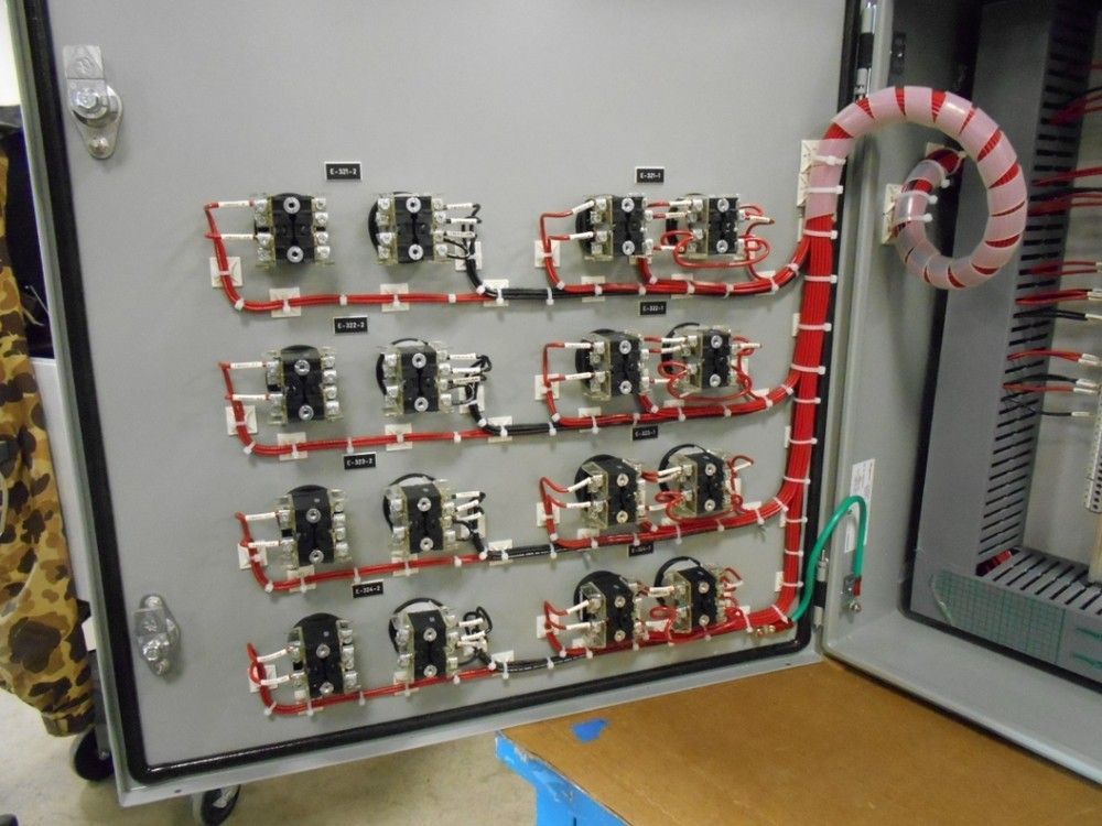 Electrical panel with rows of black switches, red and white wiring, in a gray metal enclosure.