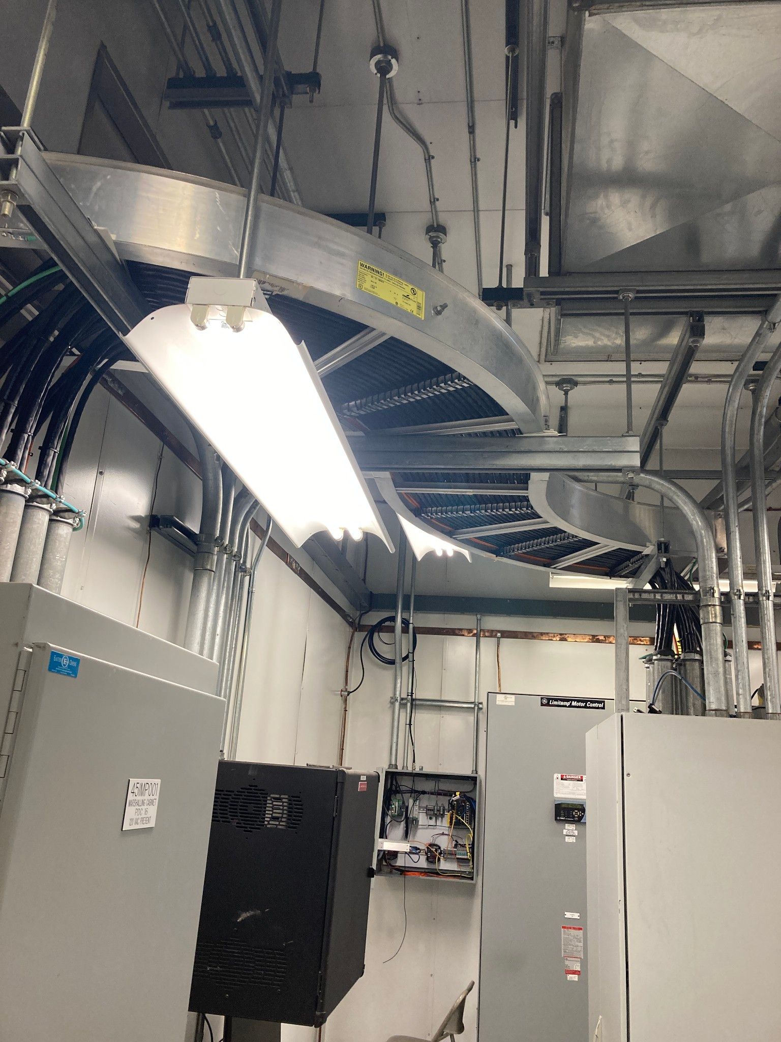 Electrical room with conduit, cable trays, lights, and electrical panels.