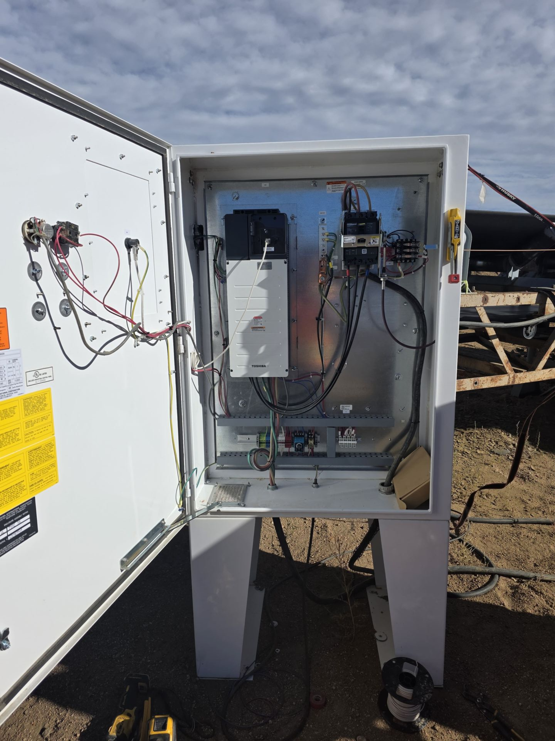 White electrical box open, revealing components and wiring, outdoors on legs.