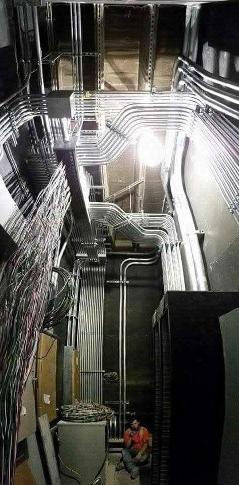 A man is sitting in a room with a lot of pipes and wires.