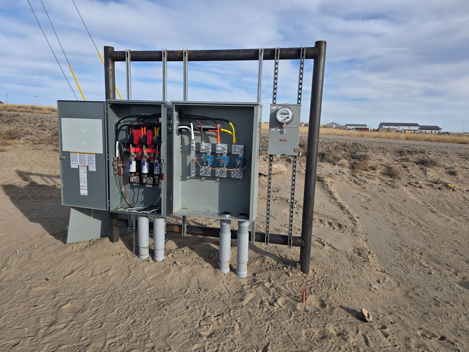 Electrical panel with open doors, mounted on a frame, in a rural outdoor setting.
