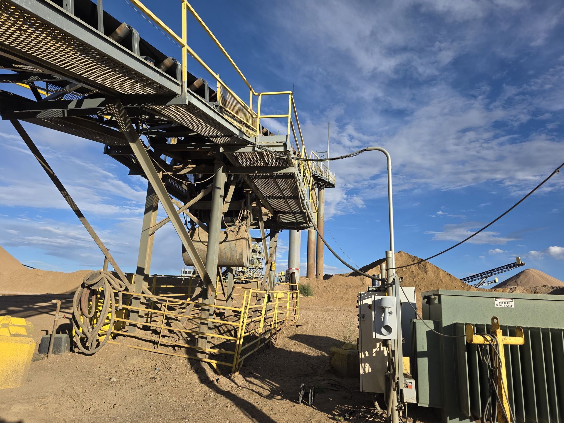 Yellow conveyor belt system at a quarry site under a partly cloudy blue sky.