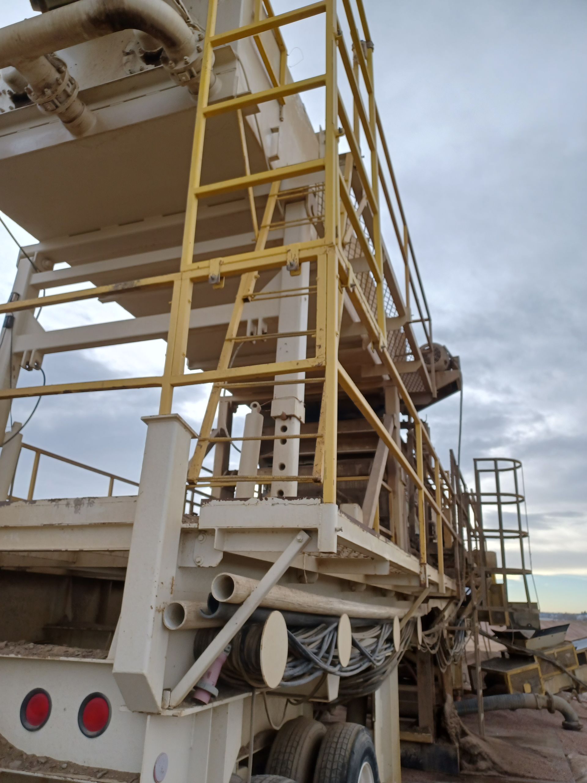 A beige industrial machine with yellow railings, likely used in construction, set outdoors.