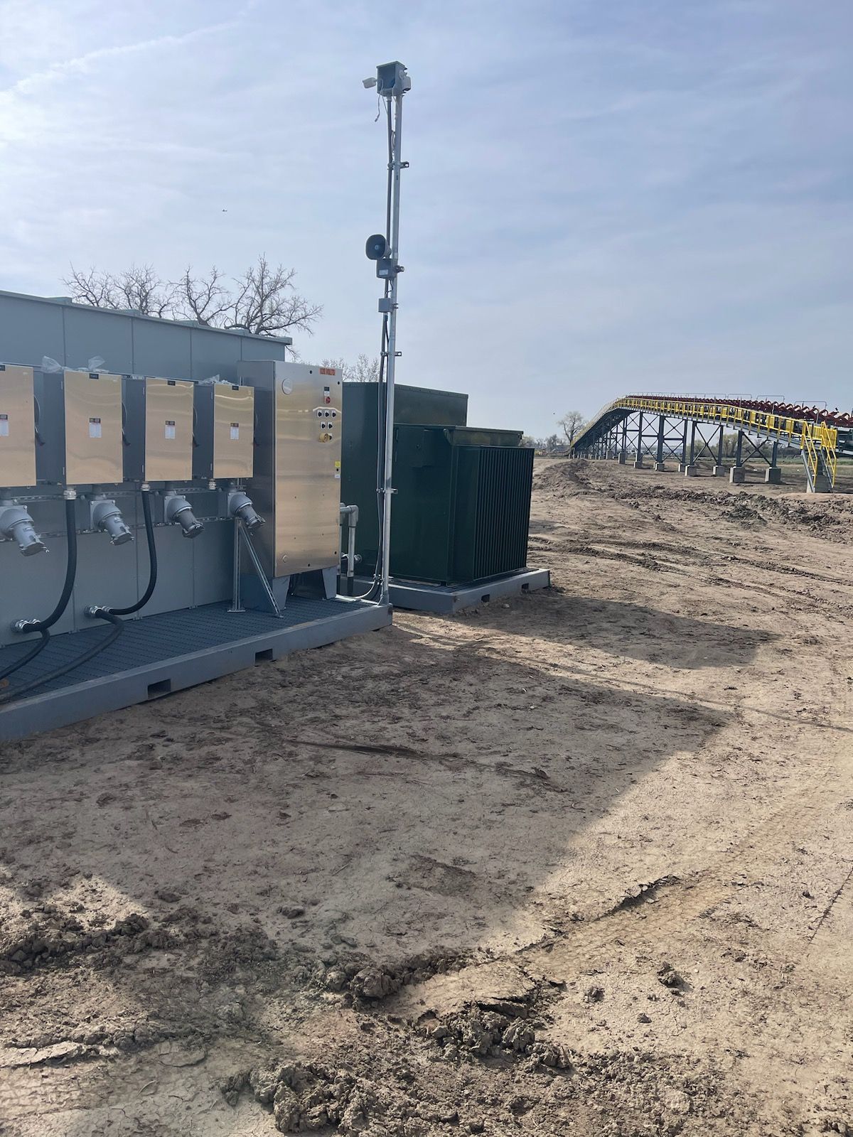 Equipment and pole in a field; a building with boxes, antennas. Solar panels in the background.