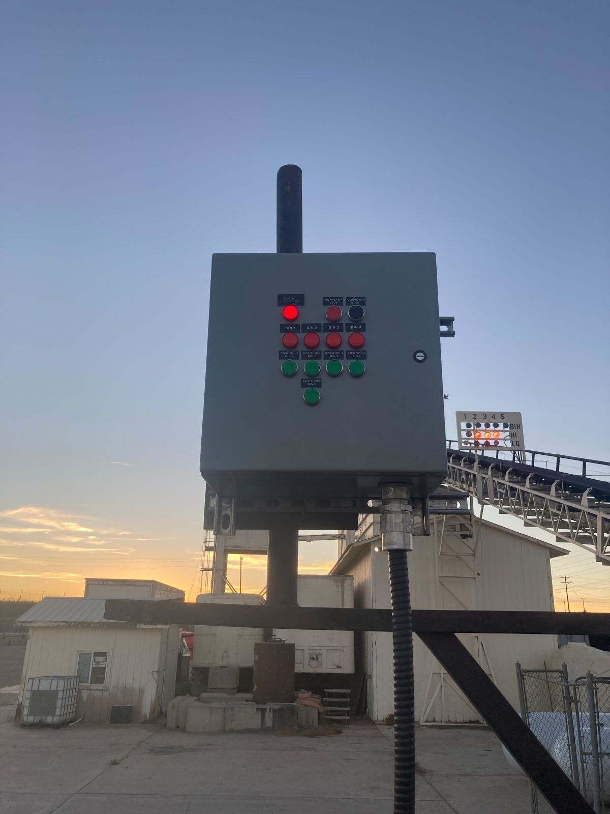 Control panel with red and green lights on an industrial site at sunset.