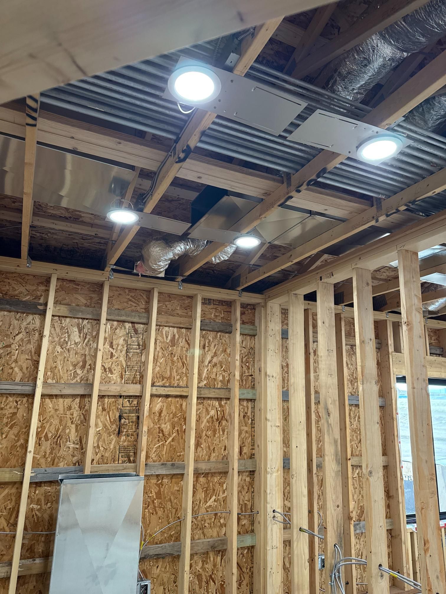 Interior view of a wood-framed room under construction, showing ceiling lights and insulation, and wood studs.