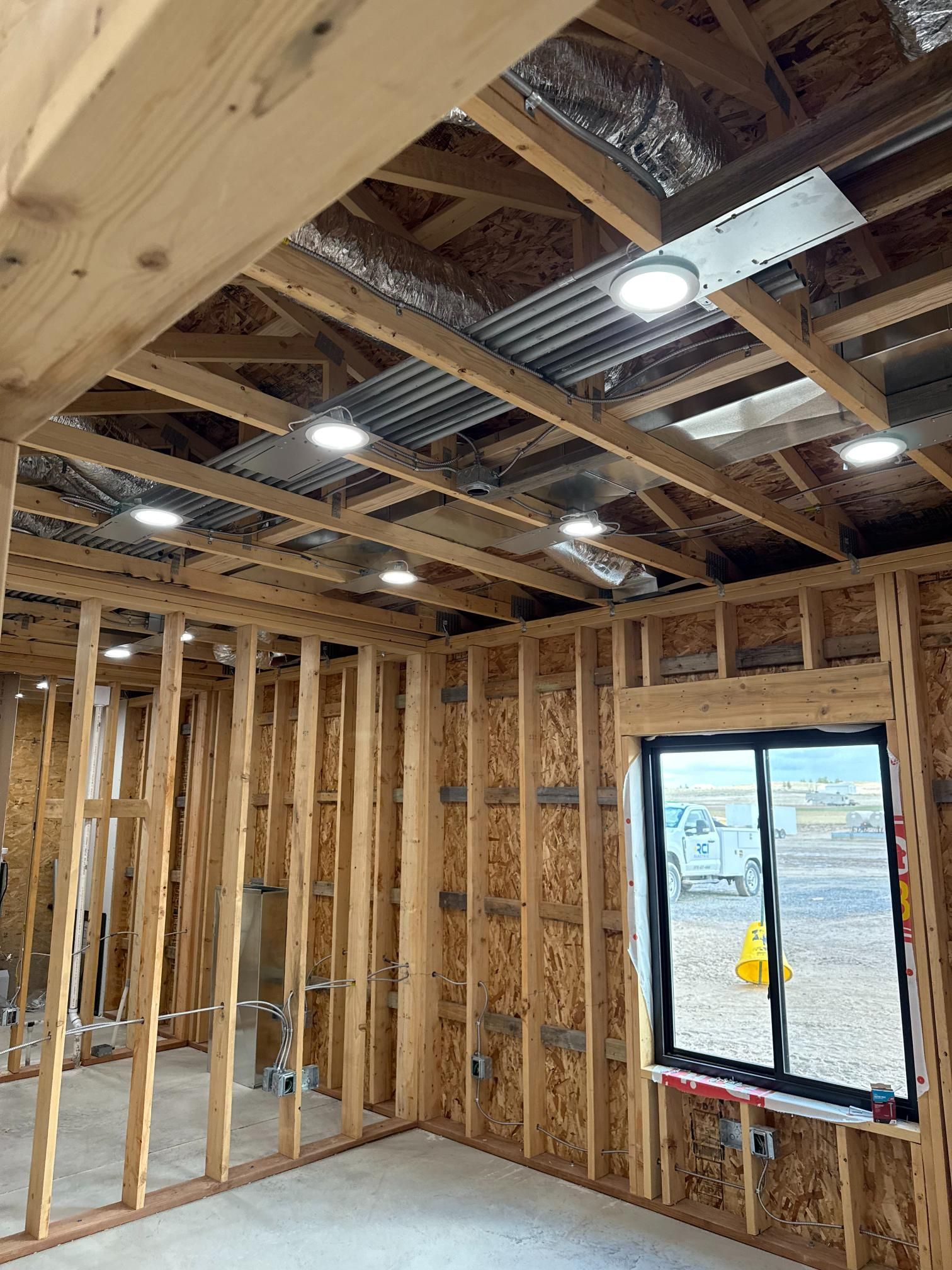 Interior view of a room under construction with exposed wooden framing and recessed ceiling lights. A window is visible.