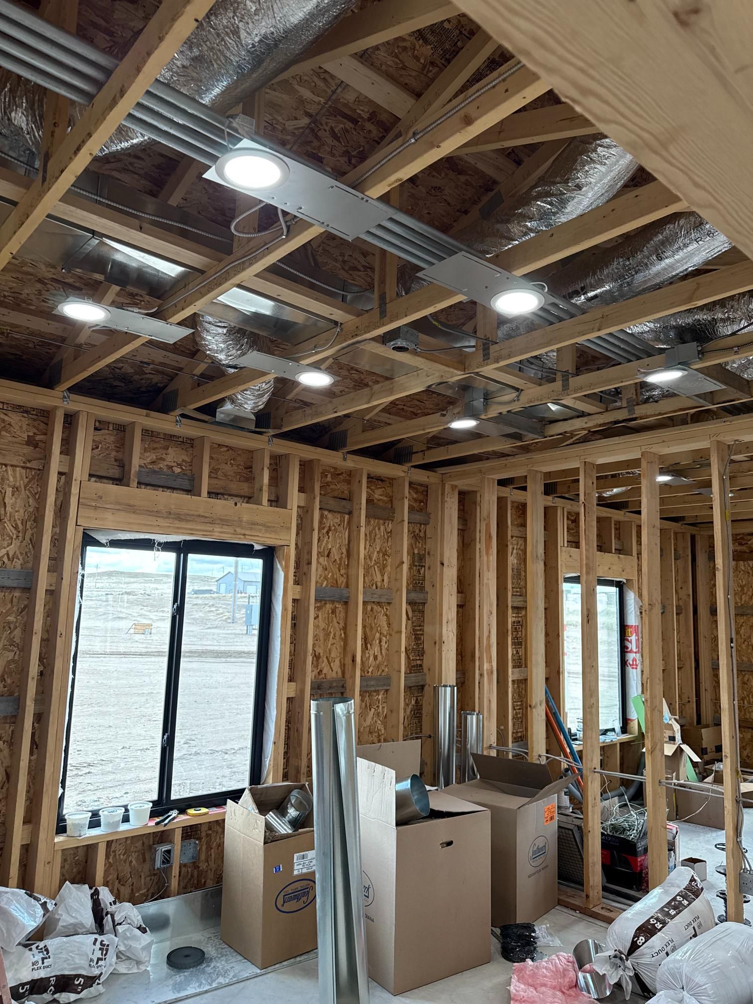 Interior view of a building under construction, showing wooden framing, ductwork, recessed lighting, and windows.