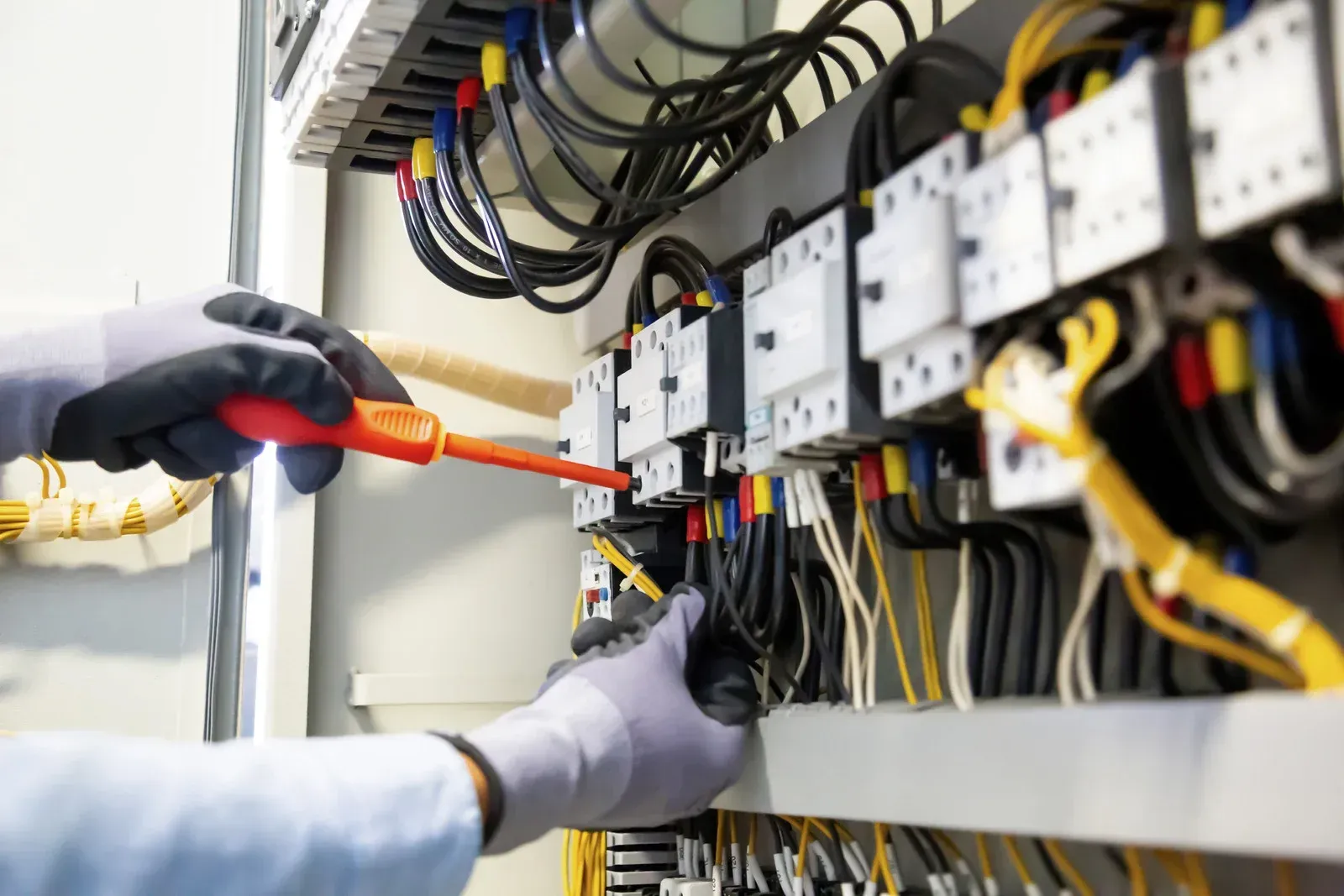 An electrician is working on an electrical panel with a screwdriver.