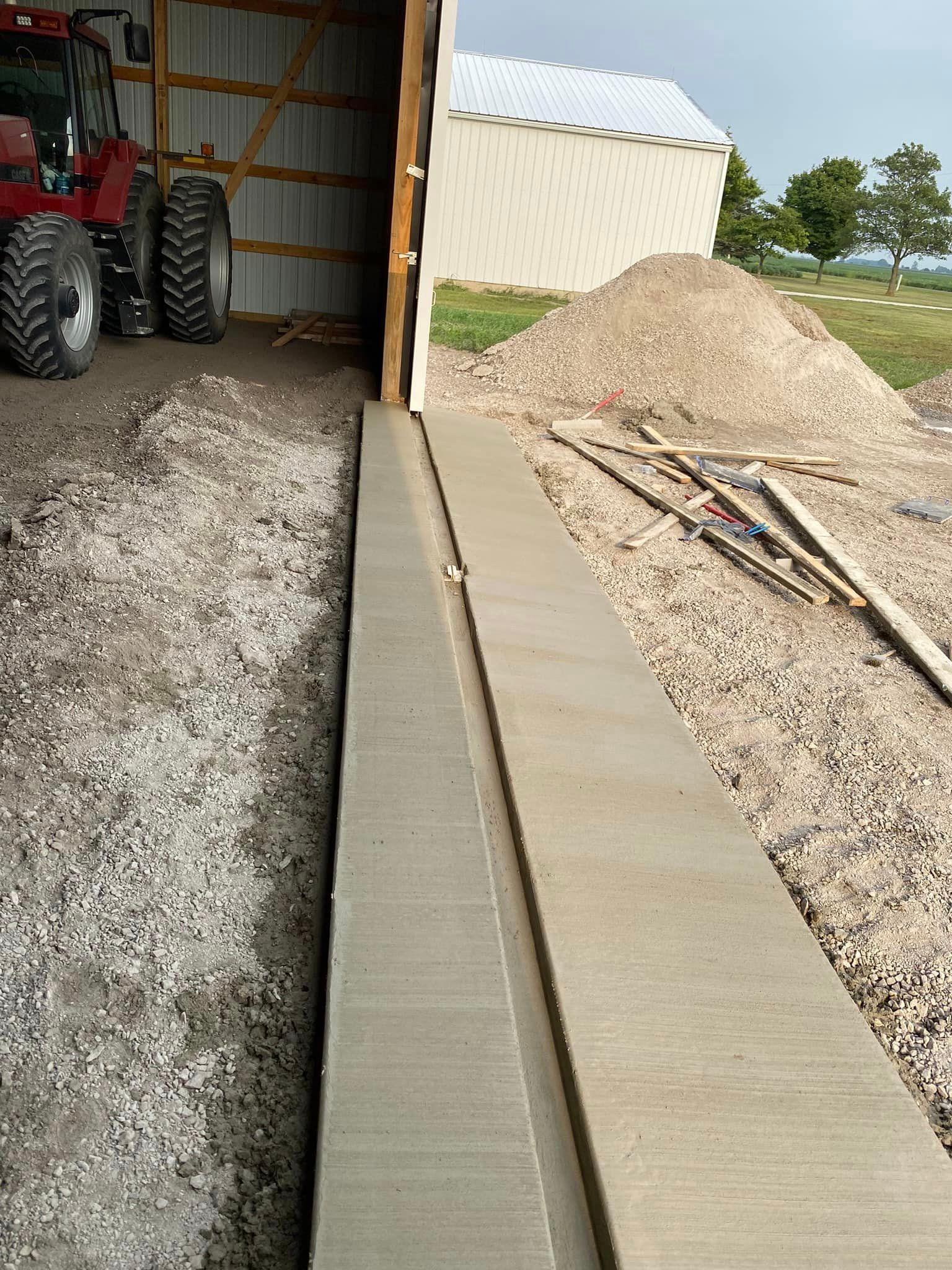 A tractor is parked in a garage next to a concrete walkway.