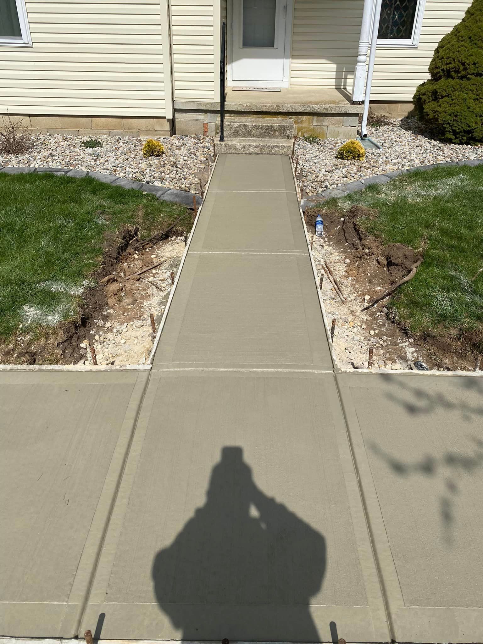 A shadow of a person is cast on a concrete walkway in front of a house.