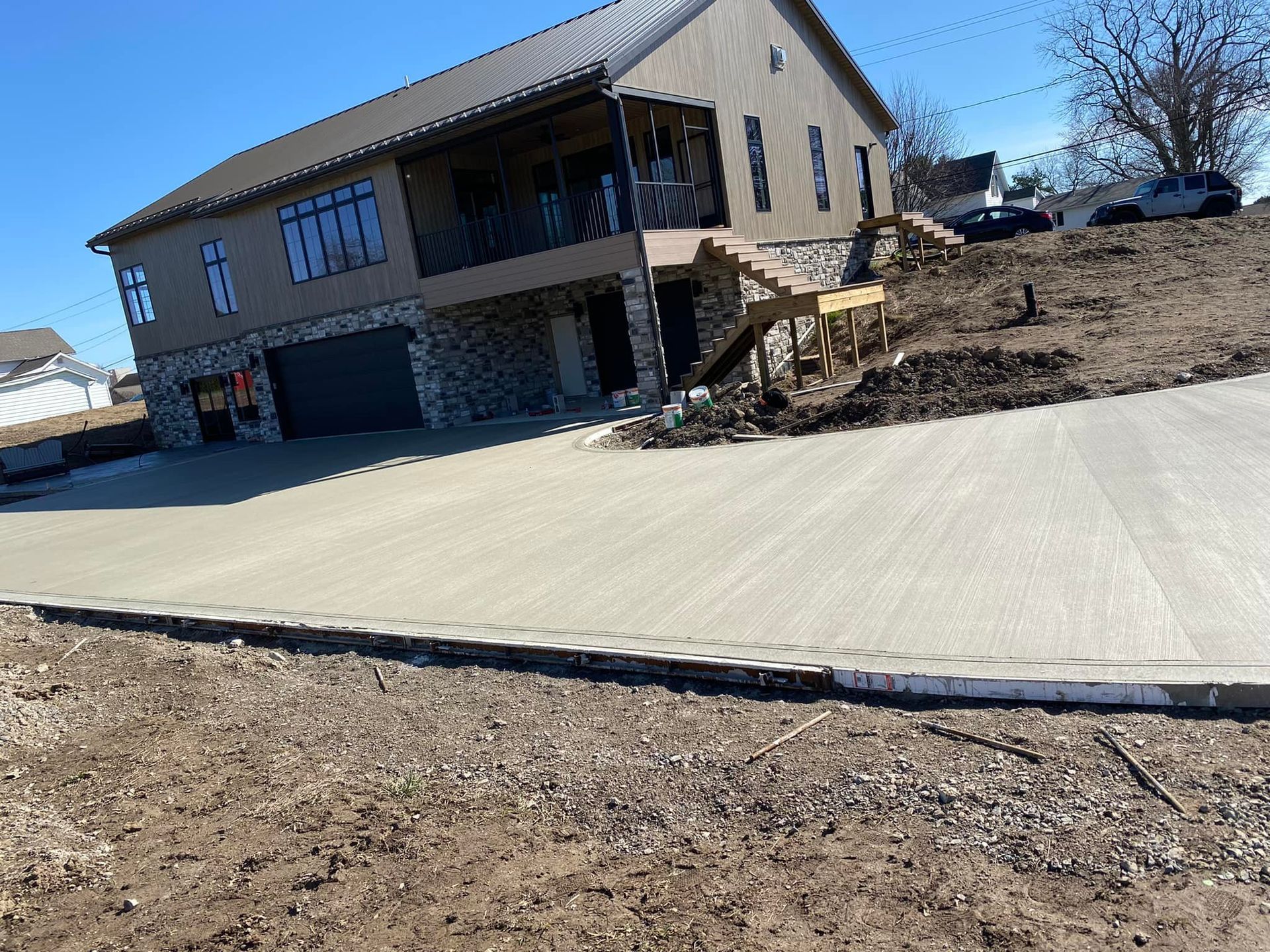A large house is sitting on top of a dirt hill next to a concrete driveway.