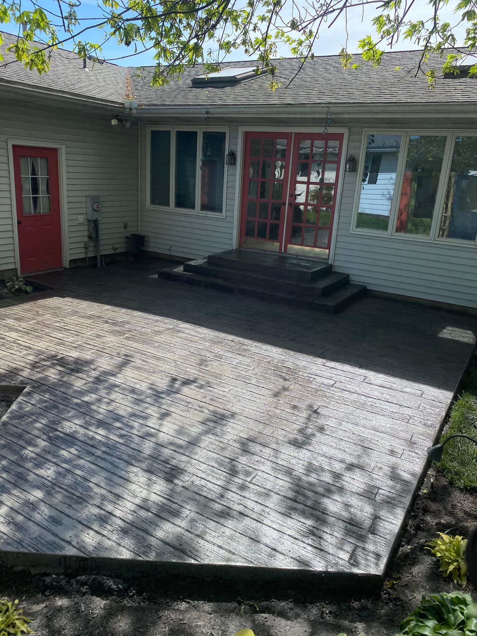 A white house with a red door and a patio in front of it.