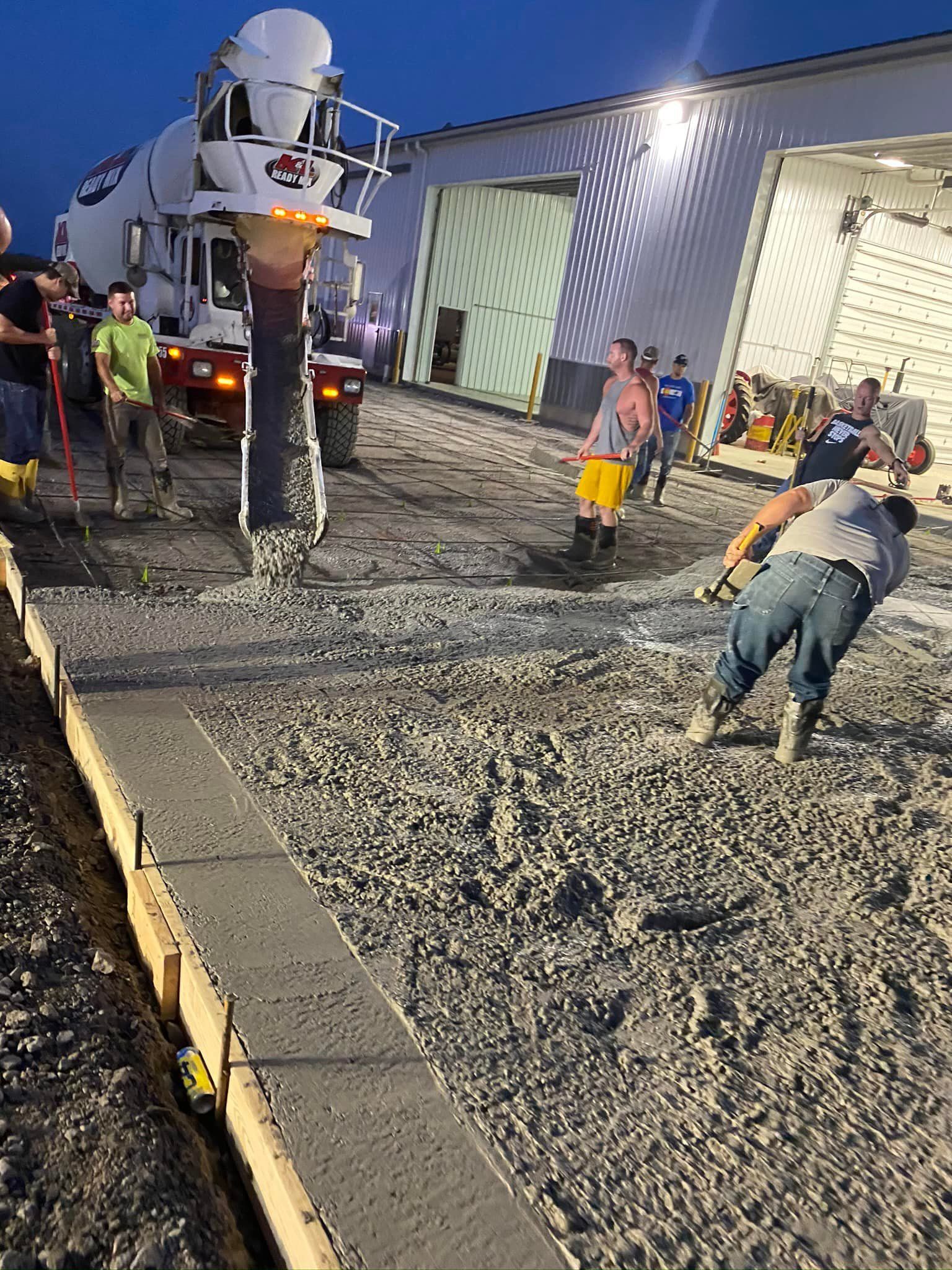 A group of construction workers are pouring concrete on a sidewalk in front of a building.