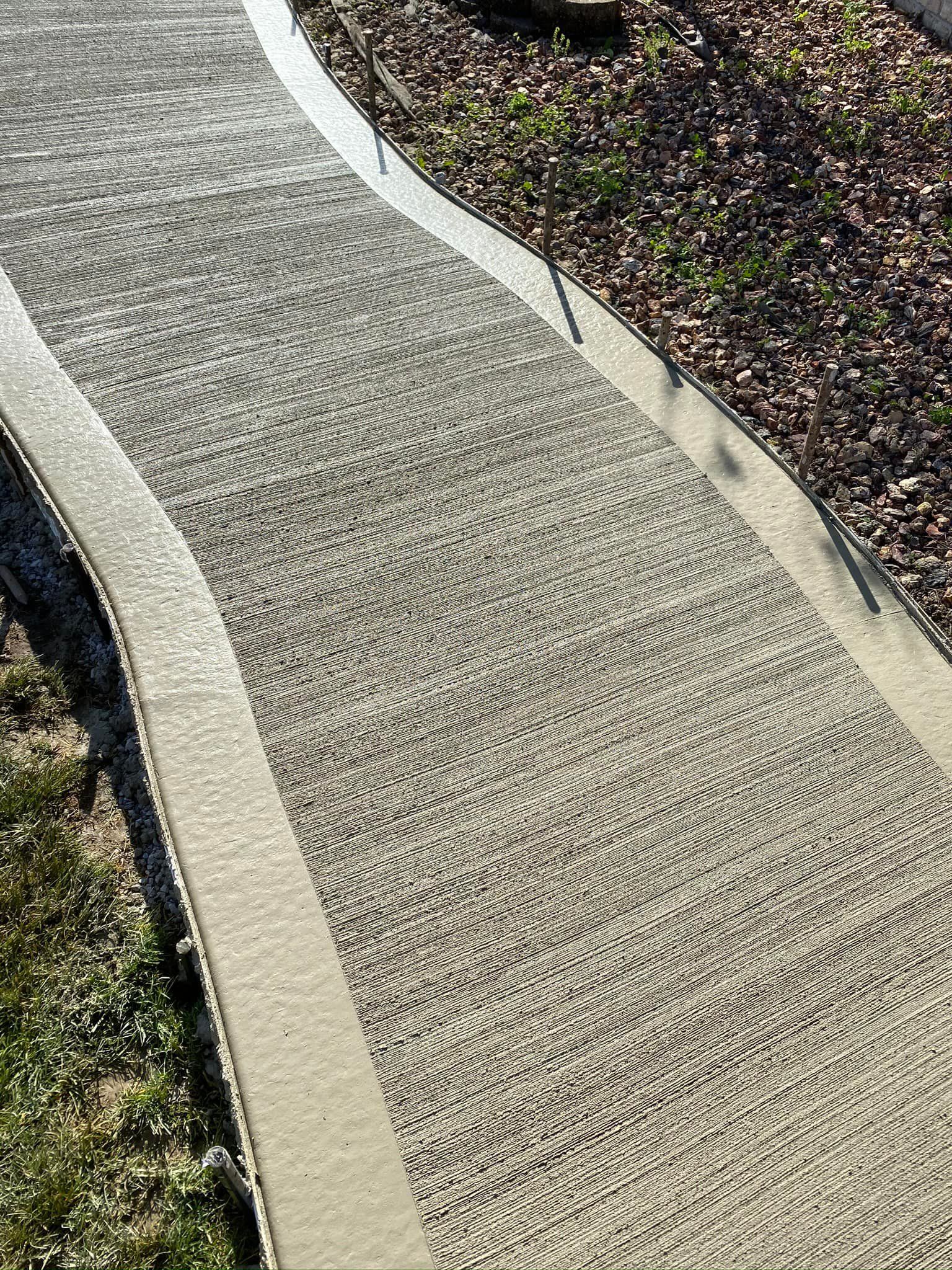 A concrete walkway with a white border is surrounded by grass and leaves.