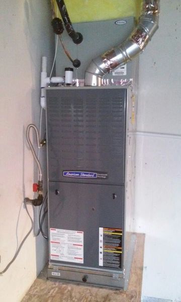 A gray American Standard furnace in a corner against a light gray wall with ductwork.