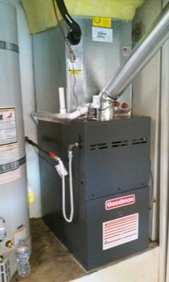 A furnace and water heater are in a utility room. The furnace is gray, Goodman brand.