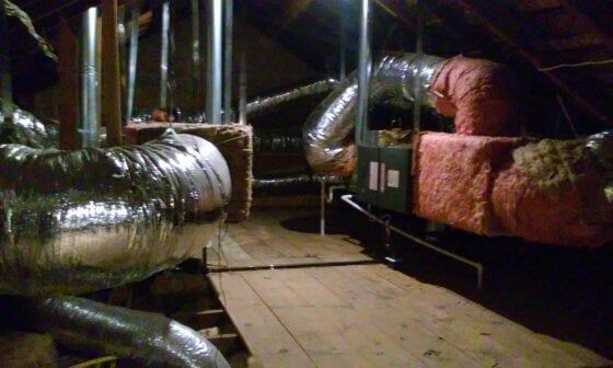 Dark attic with HVAC system, silver and insulated ducts, and wooden walkway.