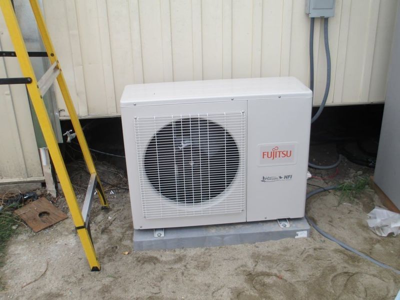 Fujitsu air conditioner unit on a concrete base, mounted outside near a building.
