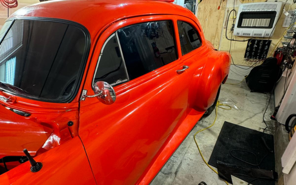 A red car is parked in a garage next to a heater.