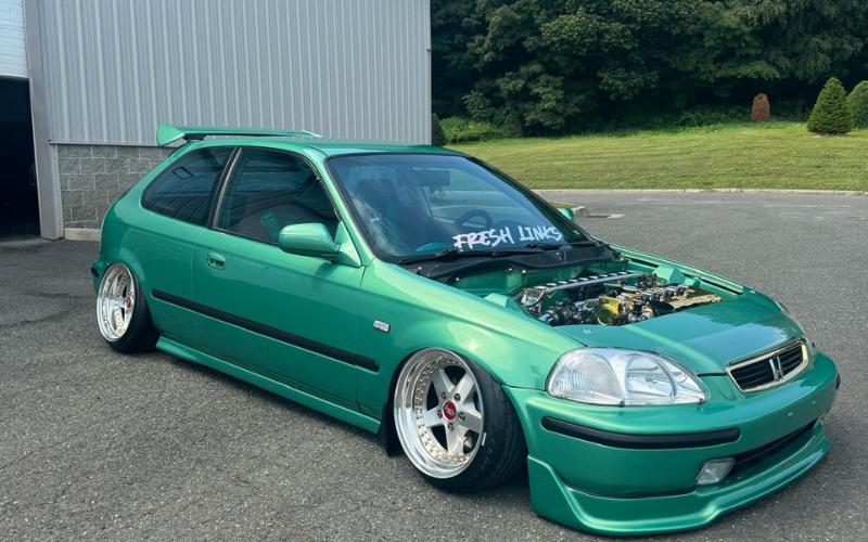 A green car with the hood up is parked in a parking lot.