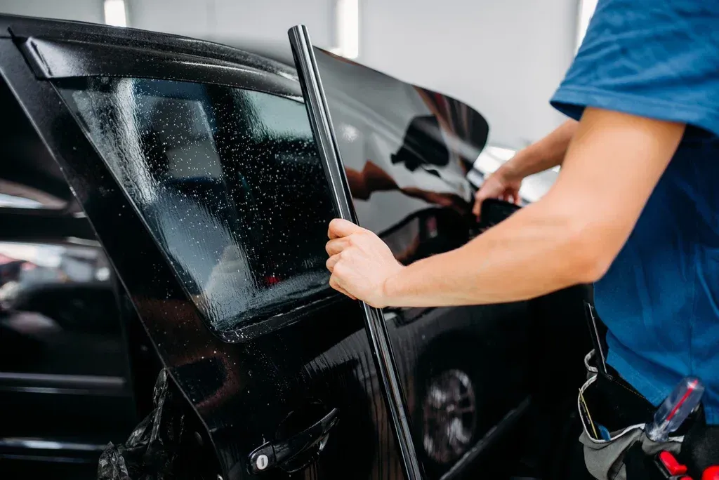 A man is applying tinted glass to a car window.