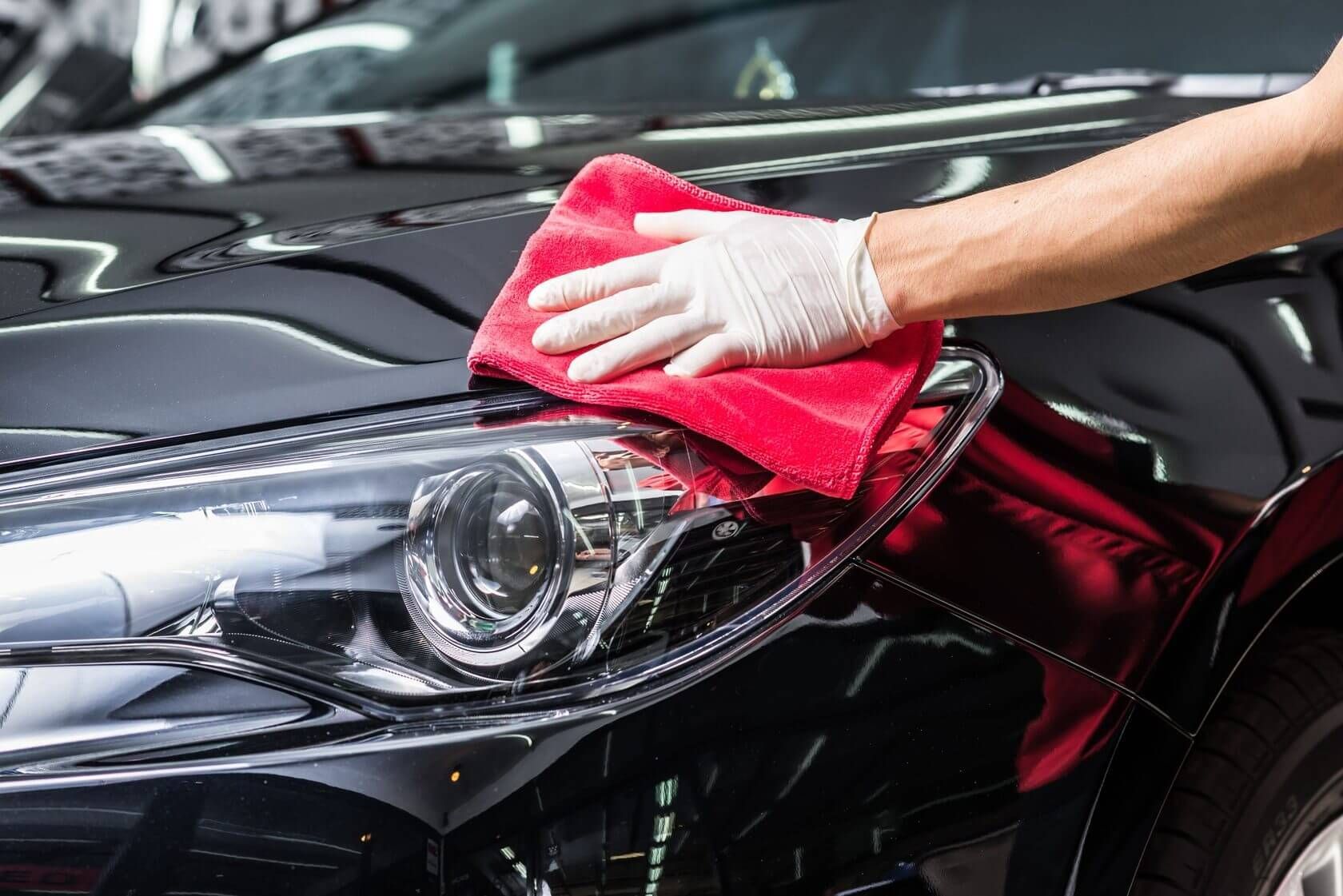 A person is cleaning a black car with a red towel.