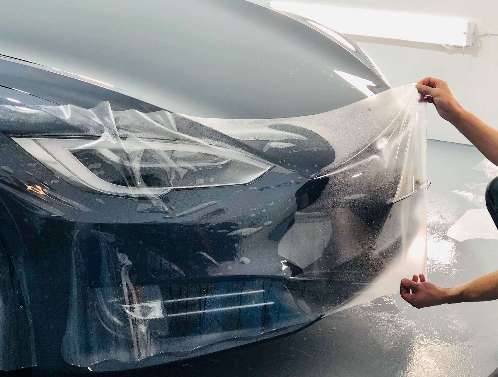 A person is covering the front of a car with plastic.