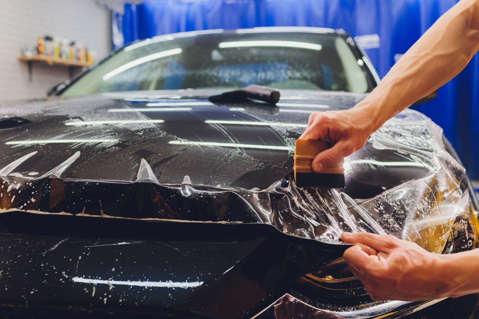 A person is applying a protective film to the hood of a car.